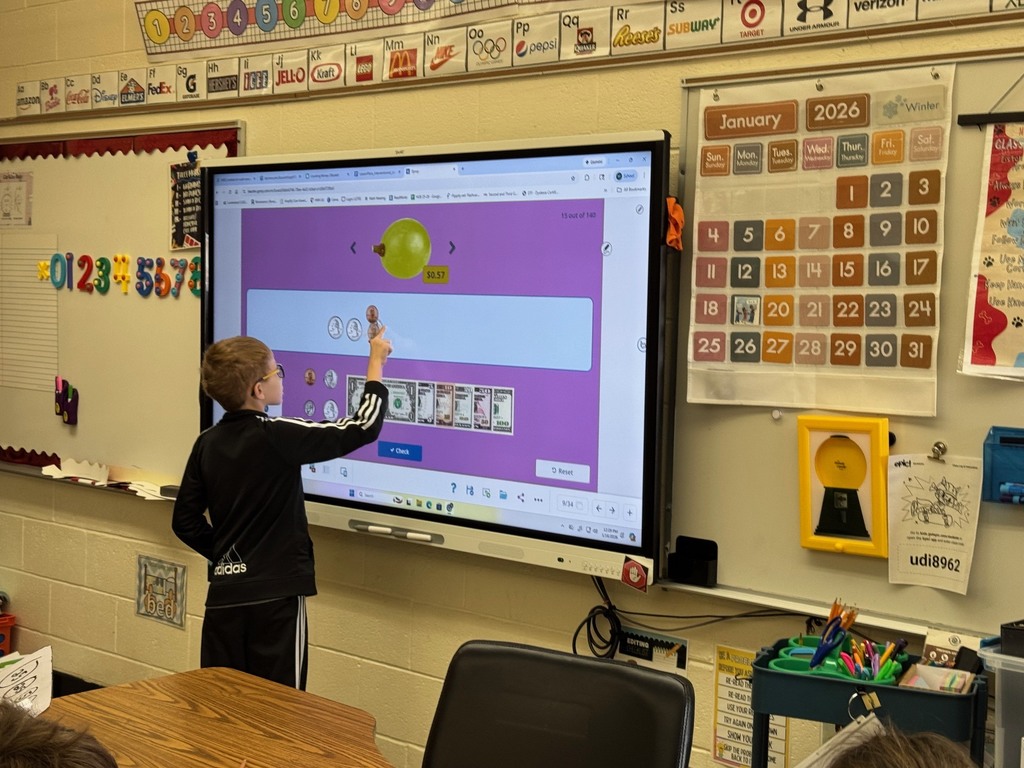 A student is standing at the Smartboard. The student is working on choosing the coins to pay for an intem.. 