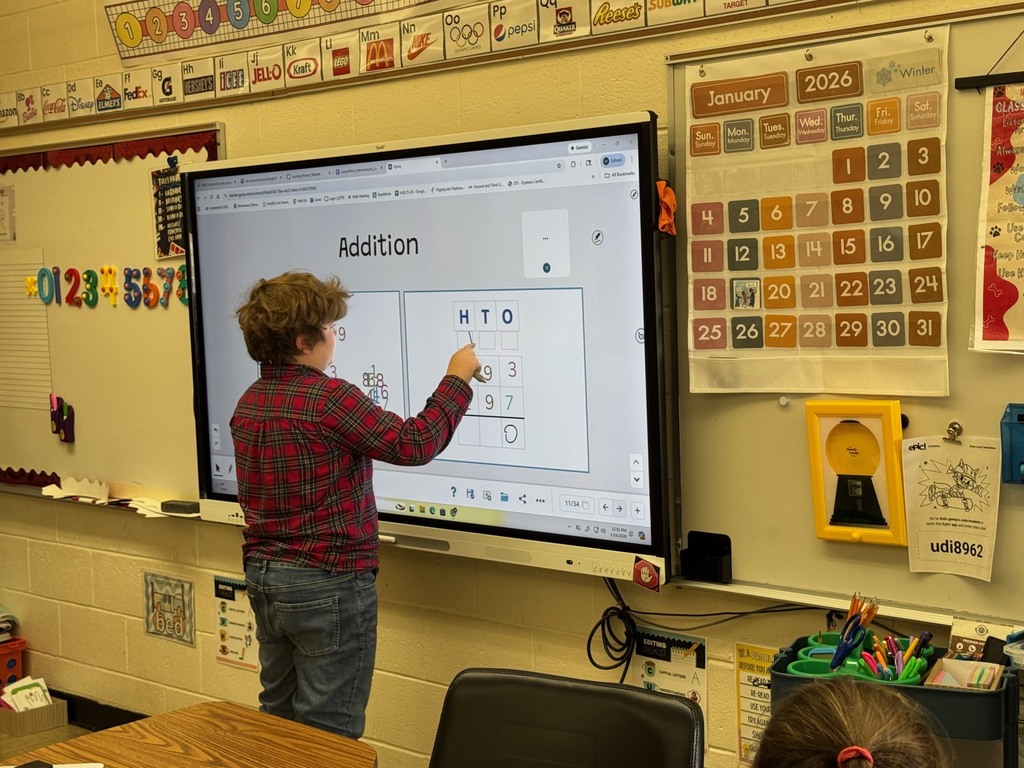 A student is standing at the Smartboard. The student is working on adding three-digit numbers. . 