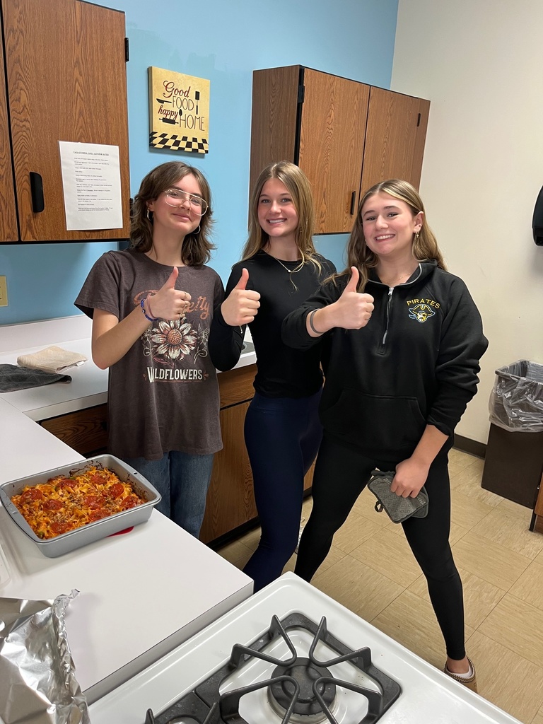 Three students are giving thumbs up. Their caserole has just come out of the oven and is cooling. 