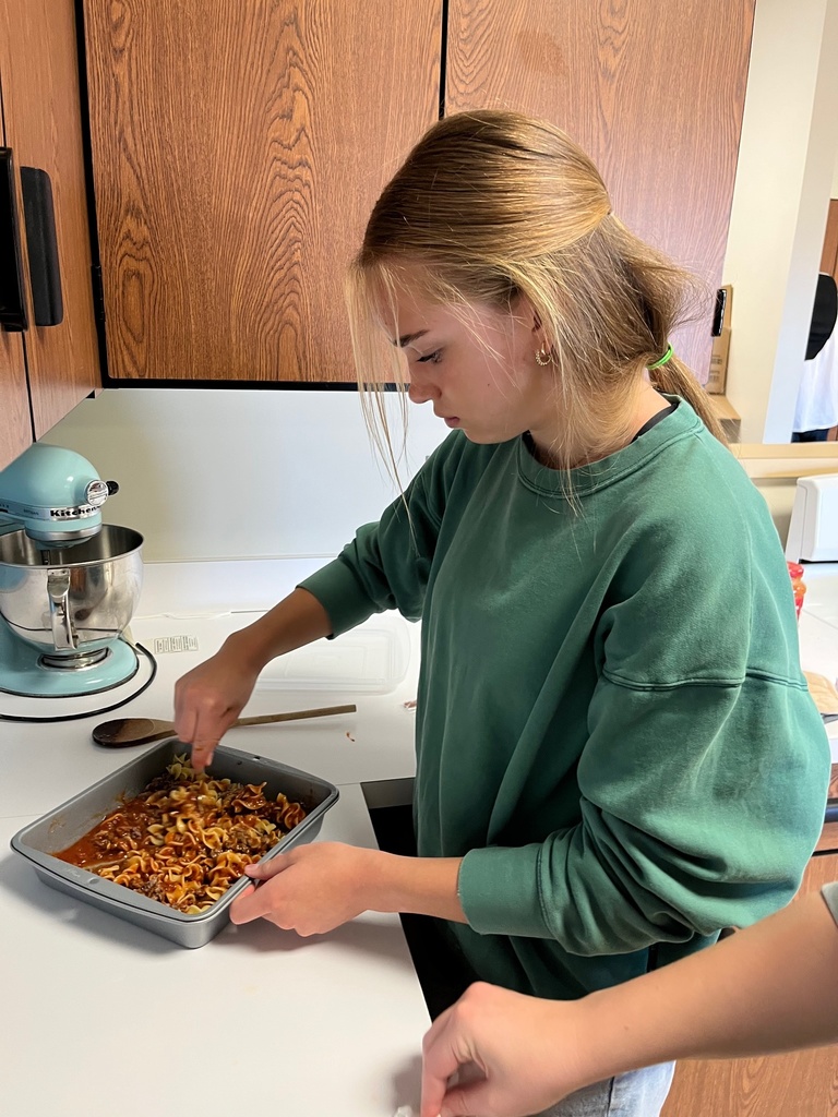 A student is at the counter. The student is adding toppings to their pizza casserole. 