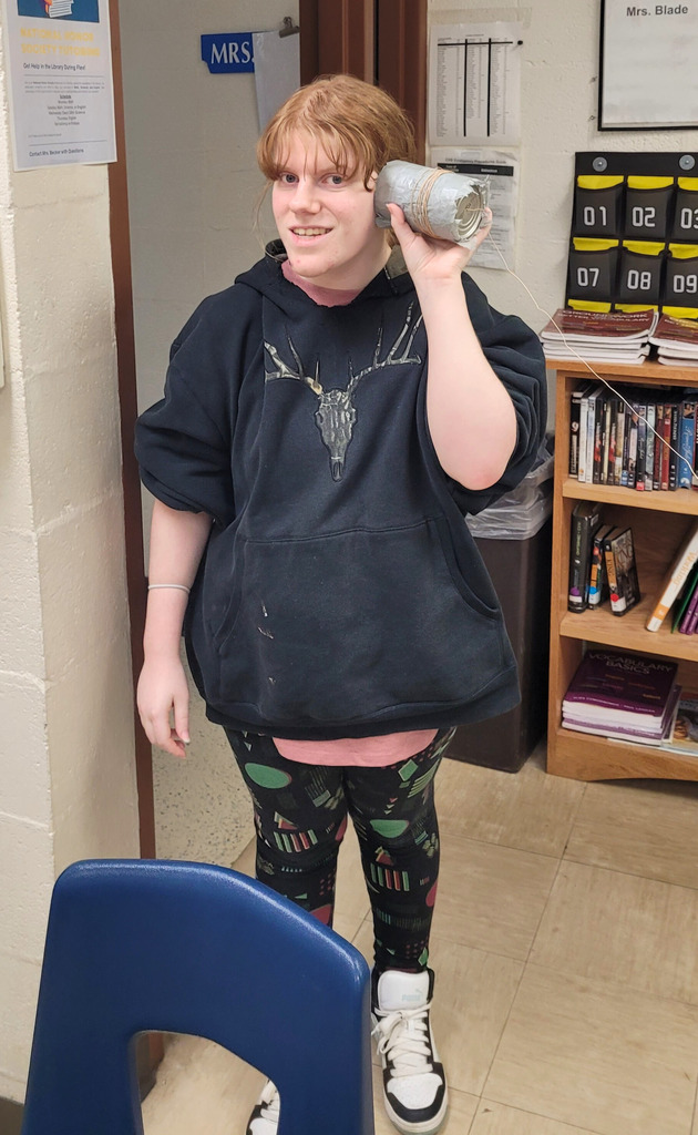 A student is listening to her phone prototype. It is a can with string attached. 
