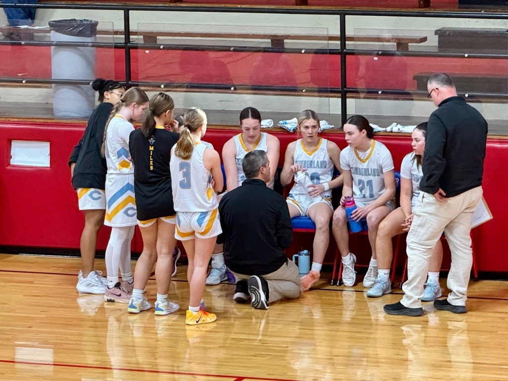The team is hudled at the bench during a time out. The coach is giving instructions. 