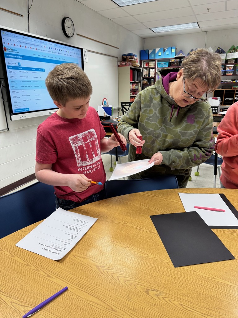 Students are holding a flashlight over a pen to create a shadow on white paper. 