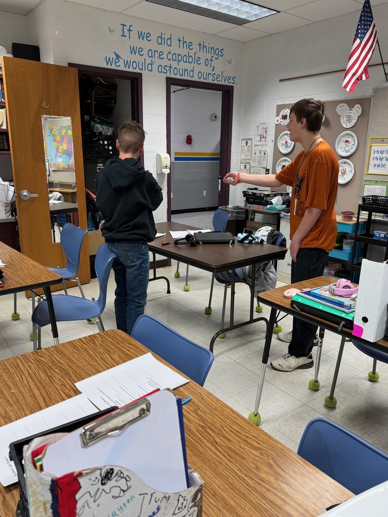 Two students are using laser pointers to shine on a mirror to see the laser refract to the wall behind them. 