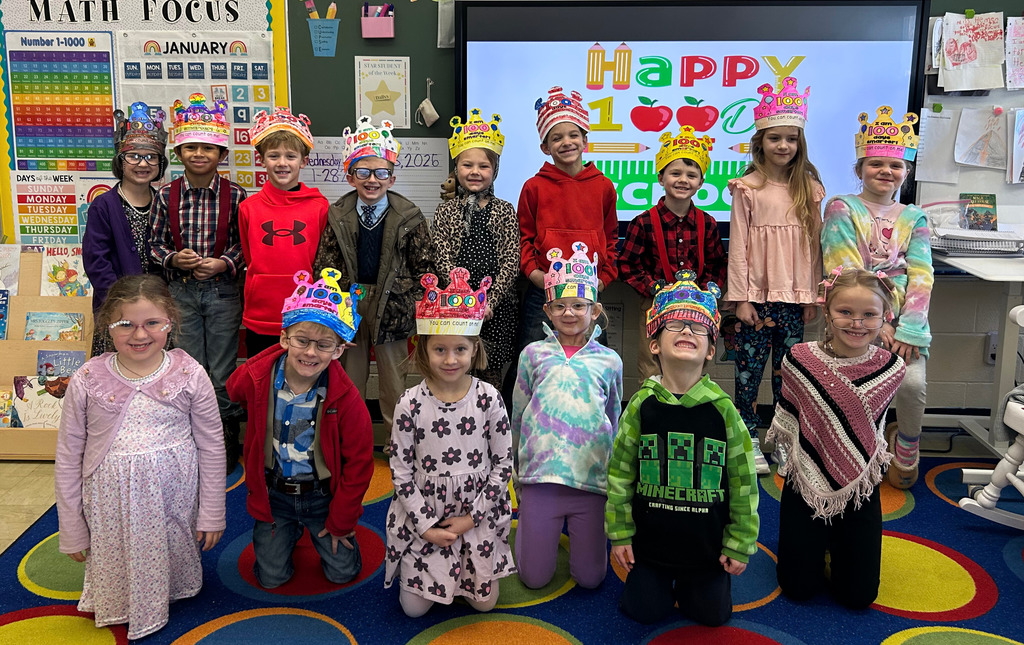 The class is together in two rows. One row is standing and another is kneeling.  They are displaying their 100 day hats. 