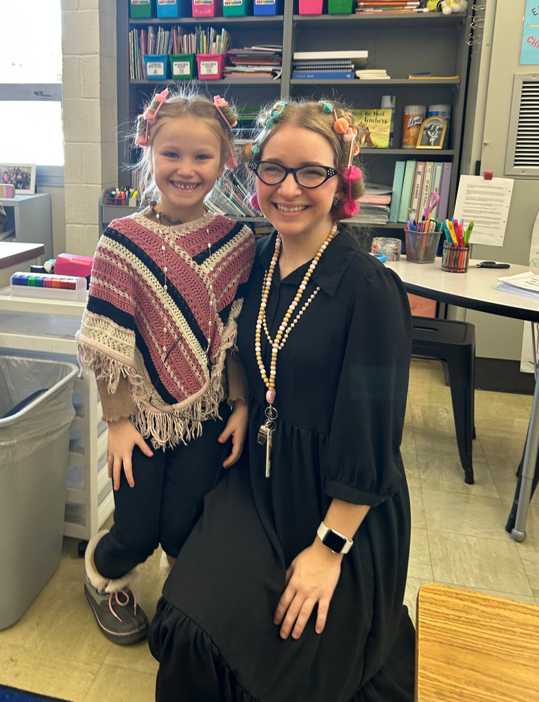 The teacher and a student are dressed like 100 year olds. Both have rollers in their hair. 