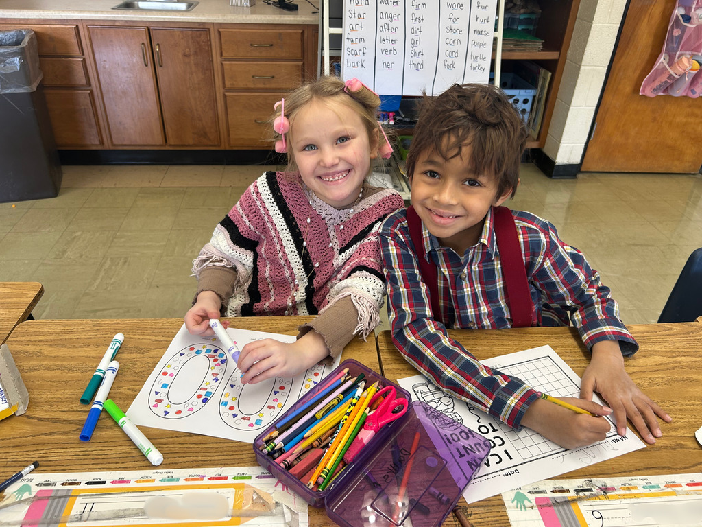 Two students are completing 100 day activities. One is coloring and another is filling out a 100 sheet. 