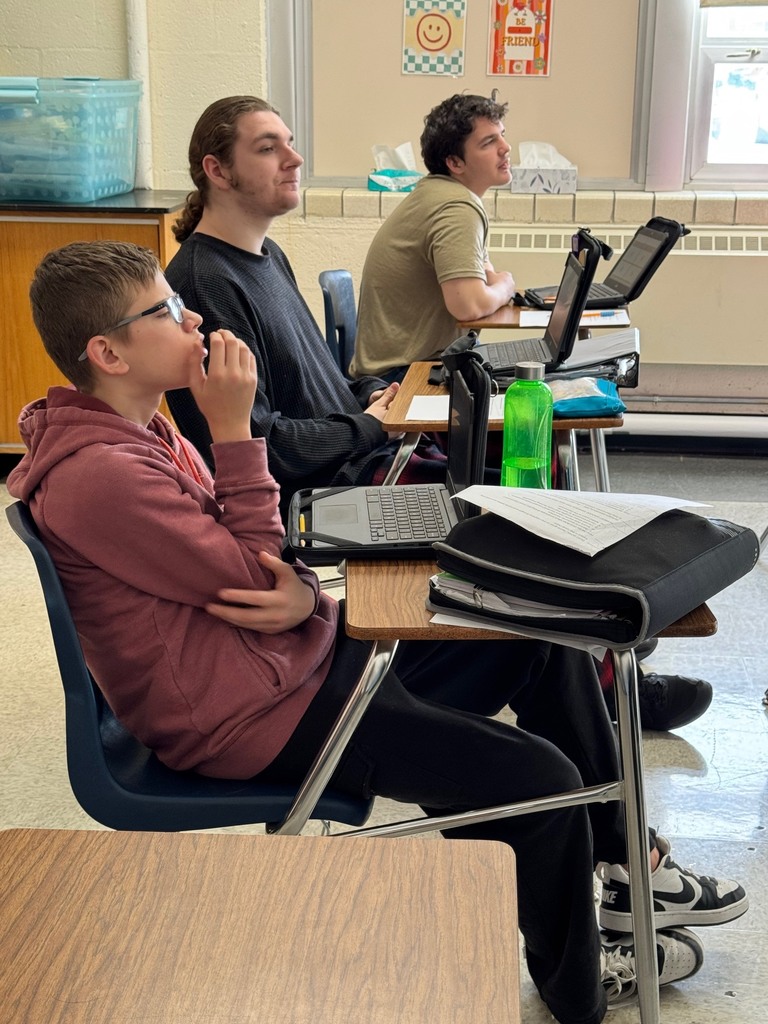 The class is sitting at their desks. They are looking at the screen or at their device, or clicking the answers to the questions.
