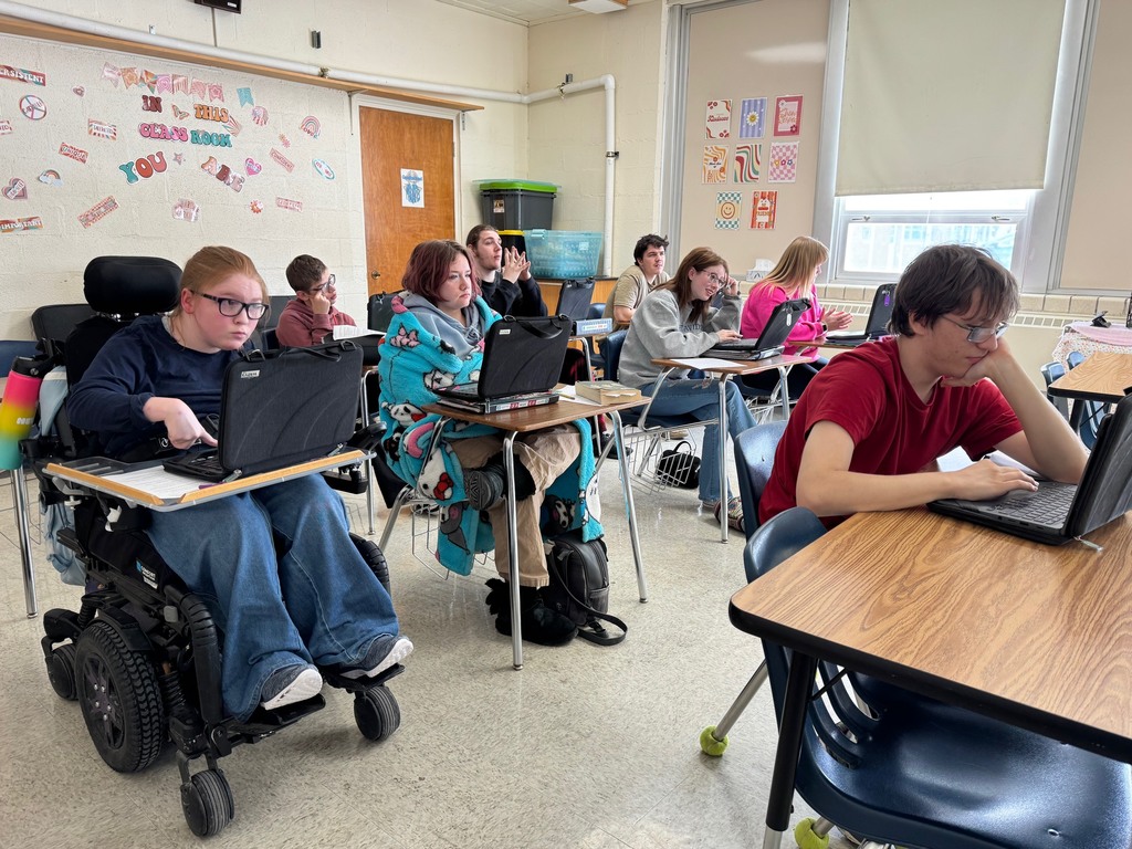 The class is sitting at their desks. They are looking at the screen or at their device, or clicking the answers to the questions.