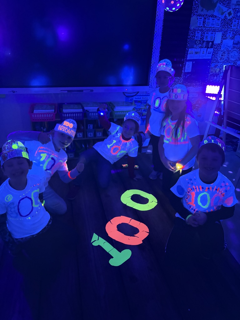 Students are sitting on the rug in the dark. They put together a 100 glow-in-the-dark puzzle. 