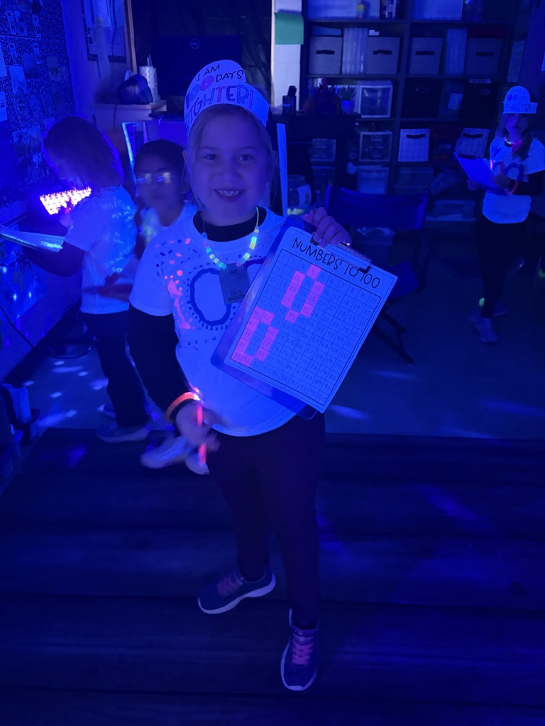 Students are standing on the rug in the dark. They are completing a 100 glowing numbers activity.