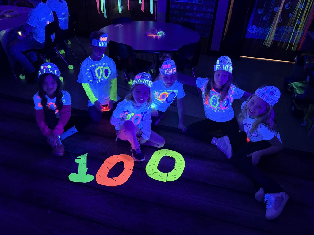 Students are sitting on the rug in the dark. They put together a 100 glow-in-the-dark puzzle. 