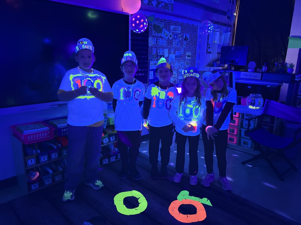 Students are standing on the rug in the dark. They put together a 100 glow-in-the-dark puzzle. 