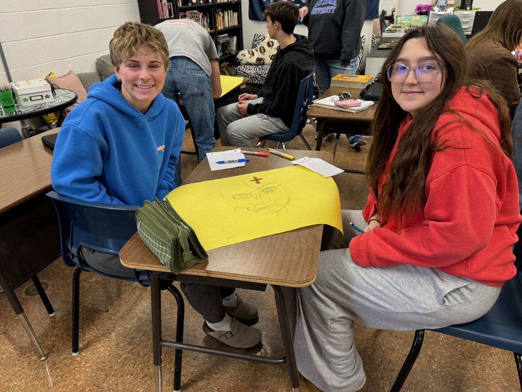 Students, working in groups are drawing one of the characters. The students are adding elements to the face. One side is what they show the world. The other side is what they hide. 