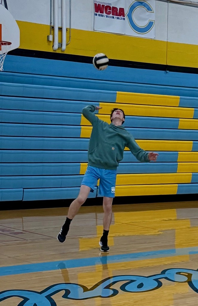 A student is overhand serving the volleyball over the net to the other team. 