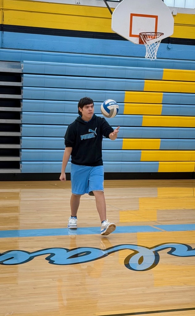 A student is underhand serving the volleyball over the net to the other team. 