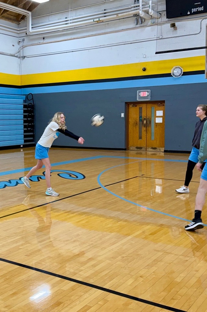 A student is bumping the volleyball over the net to the opposite side of the court. 