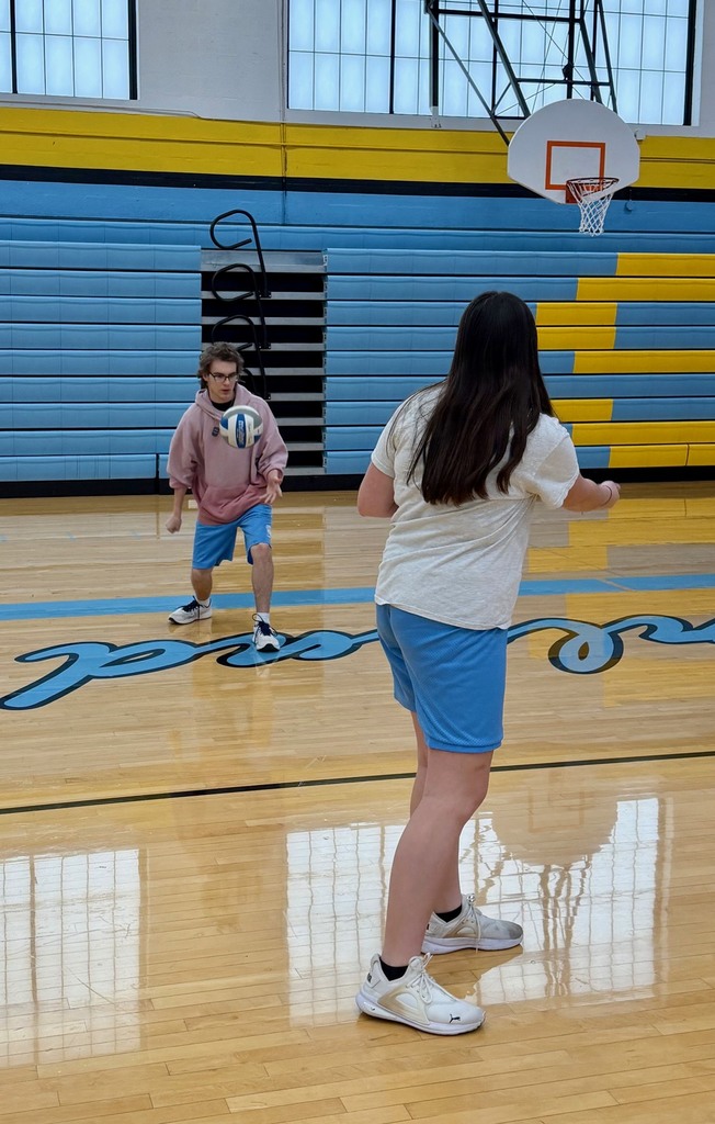A student is underhand serving the volleyball over the net to the other team. 