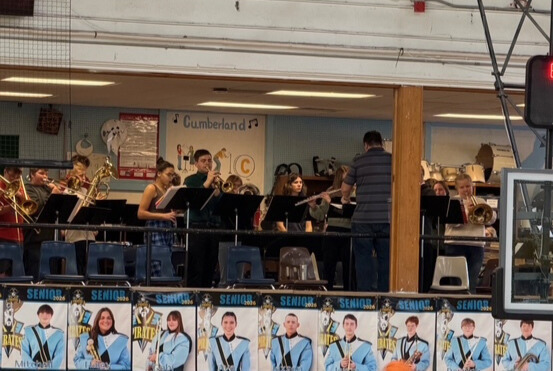 The band is playing in the loft. They are standing behind  stands and being directed by Mr. O. 