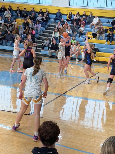A basketball player is going up for a jump shot in the land. She is being defended by one opposing player.