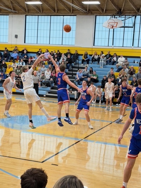 A basketball player is going up for a jump shot. He is being defended by one opposing player.