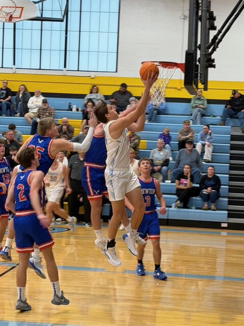 A basketball player is going up for a right handed layup. He is between several opposing team players. 