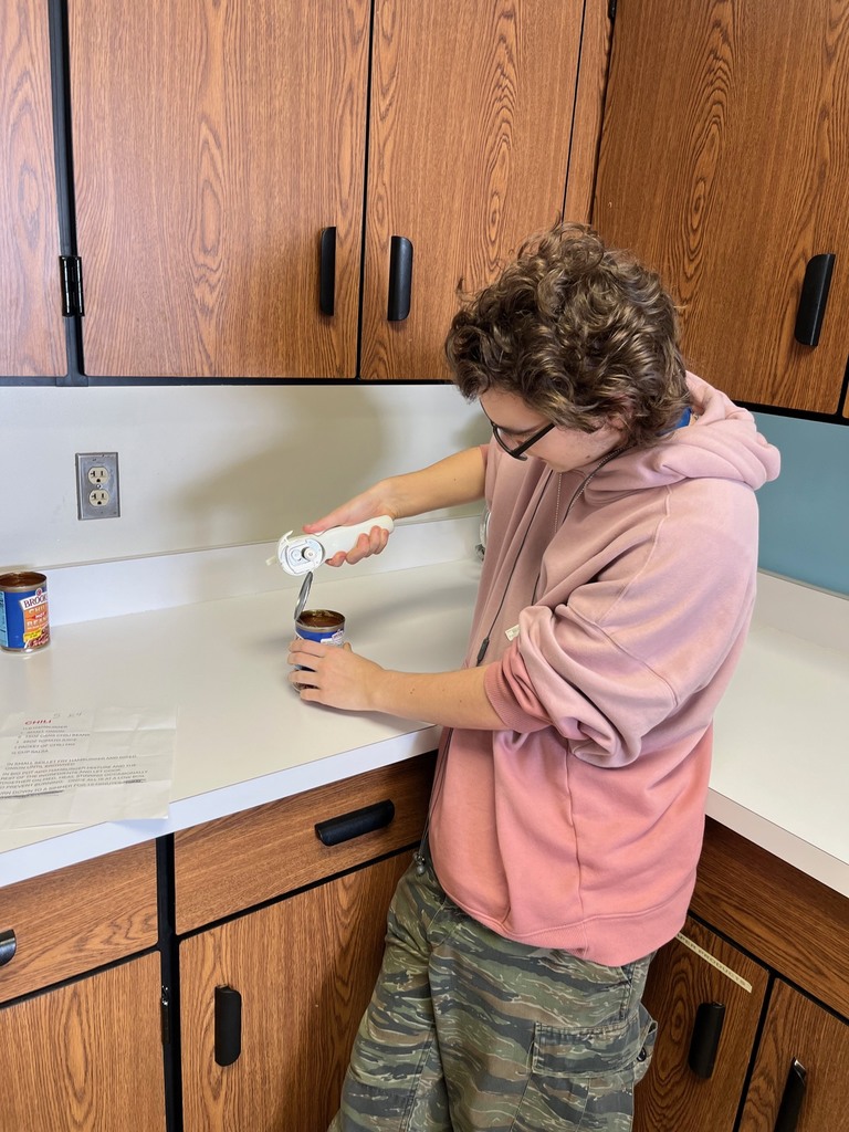 A student is using a can opener to open a can of tomato paste.