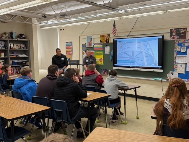 Two speakers are discussing their careers with a group of students sitting in their desks. There is a presentation on the screen. 
