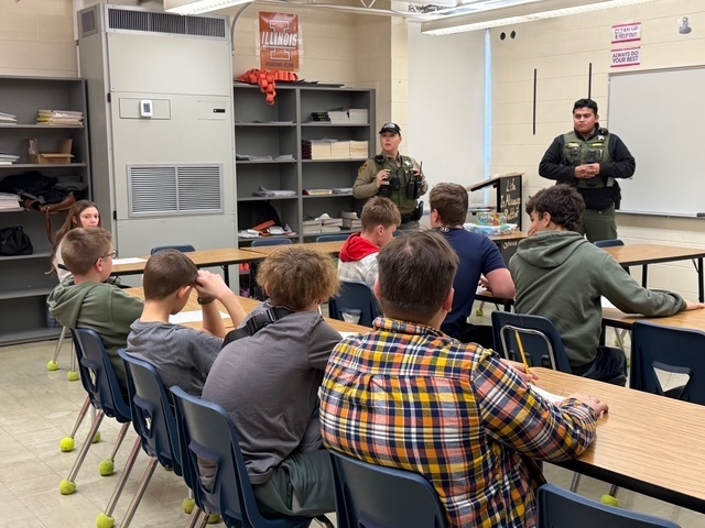 Two speakers are discussing thier careers with a group of students sitting at tables. 
