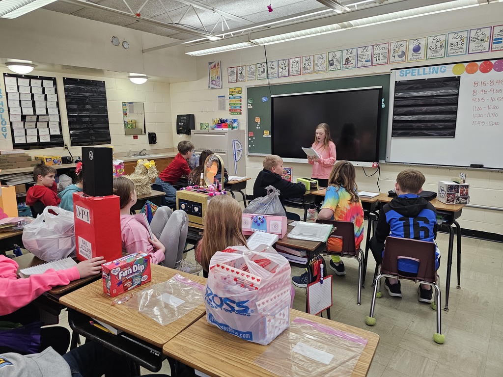 A student is standing in front of the class sharing her work. The class is listening to her speak.