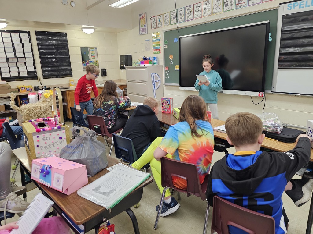 A student is standing in front of the class sharing her work. The class is listening to her speak.