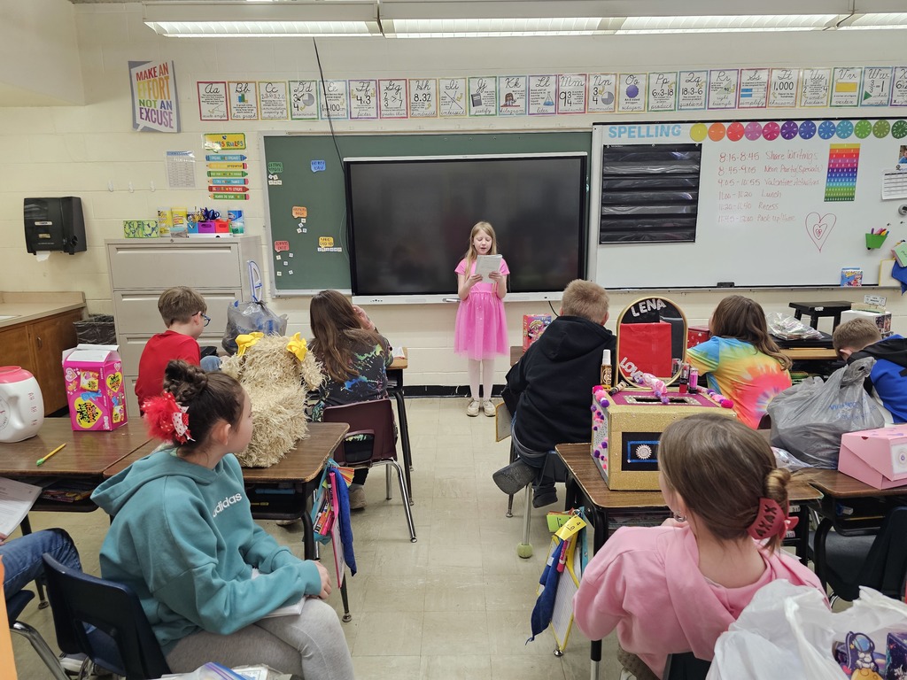 A student is standing in front of the class sharing her work. The class is listening to her speak.