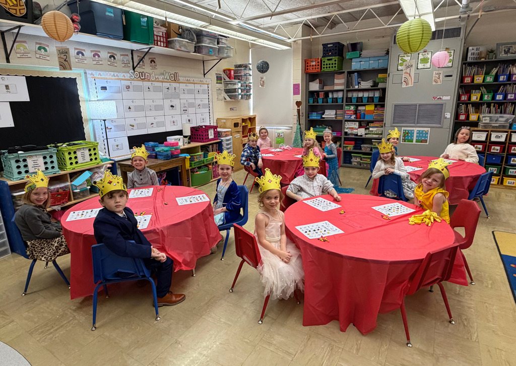 The students are sitting at their tables which are cover with a red tablecloth. They are wearing fancy clothing and a crown.