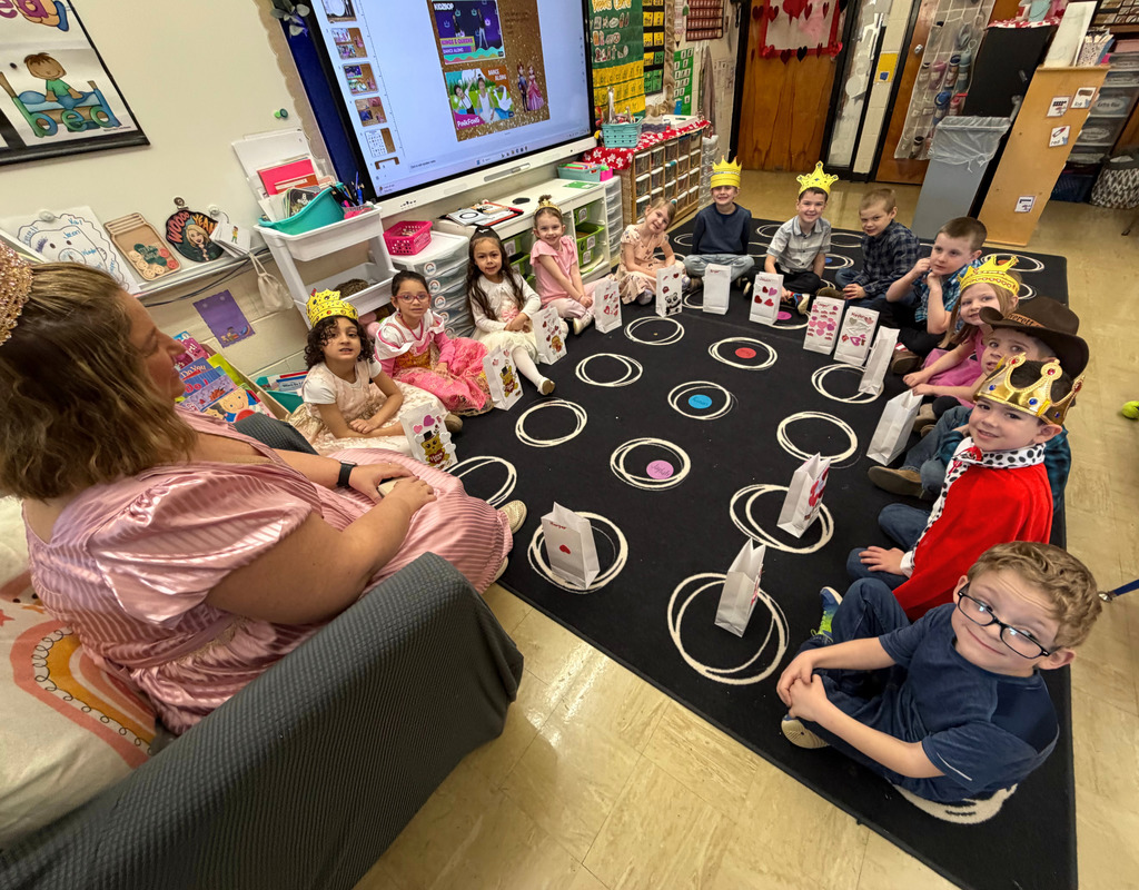 The students are sitting on the carpet. They are wearing fancy clothing and a crown.
