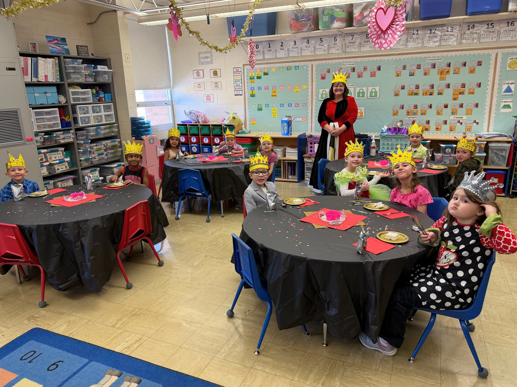 The students are sitting at their tables which are cover with a black tablecloth. They are wearing fancy clothing and a crown.