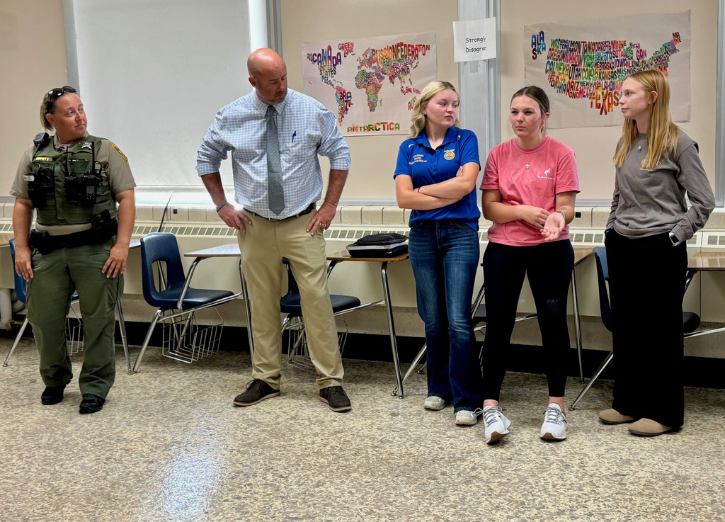 Officer E is standing with the superintendent and three students. They are discussing their oppinions about gun safety.