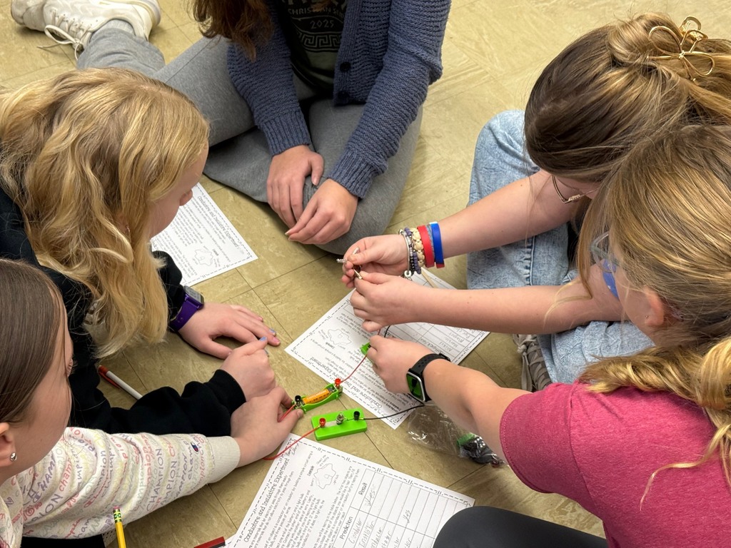 Students are in their desks with their circuit. They are adding an everyday object to the circuit to see if the bulb lights,  They are writing their results on their lab sheet. 