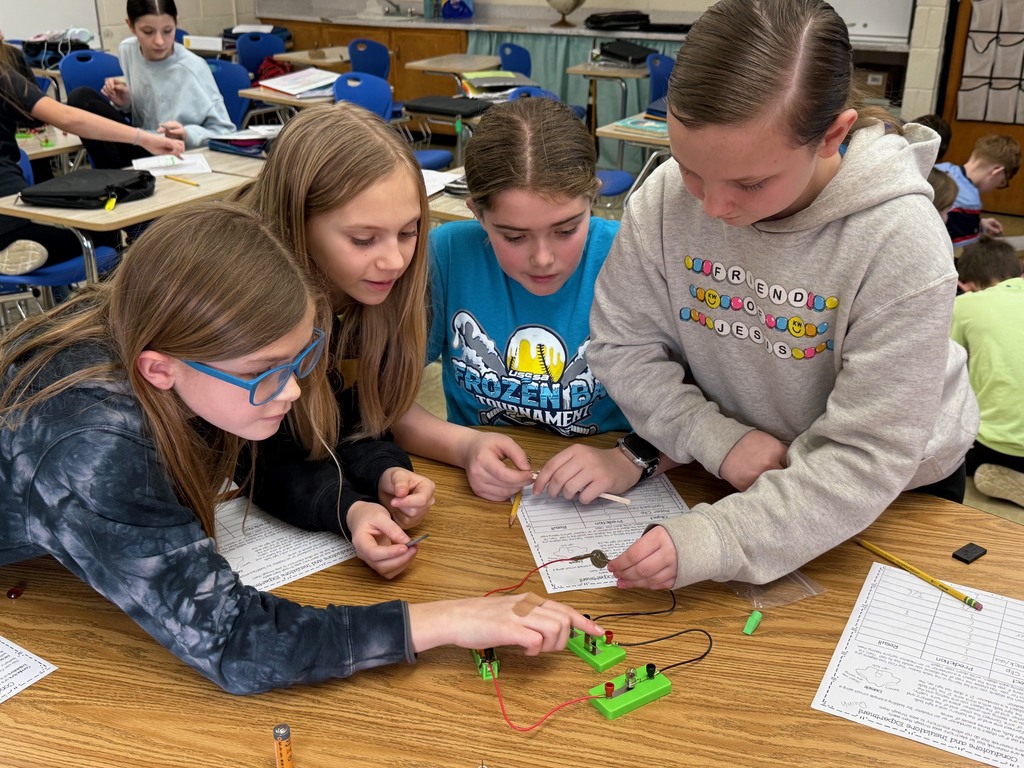 Students are in their desks with their circuit. They are adding an everyday object to the circuit to see if the bulb lights,  They are writing their results on their lab sheet. 