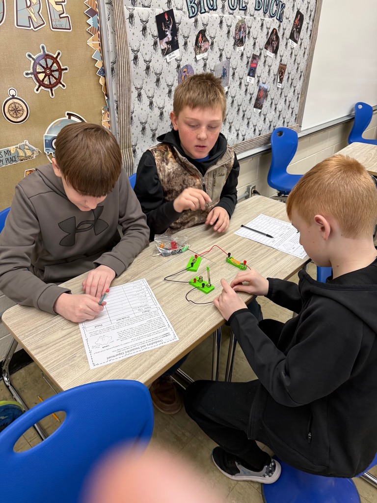 Students are in their desks with their circuit. They are adding an everyday object to the circuit to see if the bulb lights,  They are writing their results on their lab sheet. 