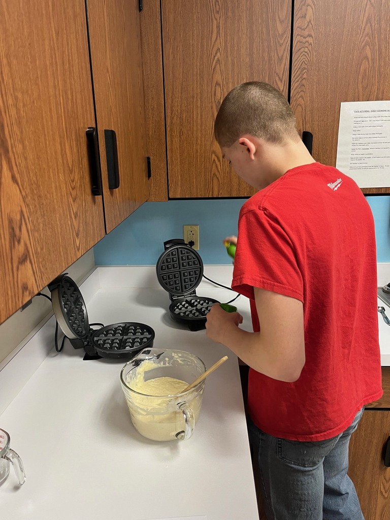 A student is spraying two waffle grills with a can of cooking oil. 