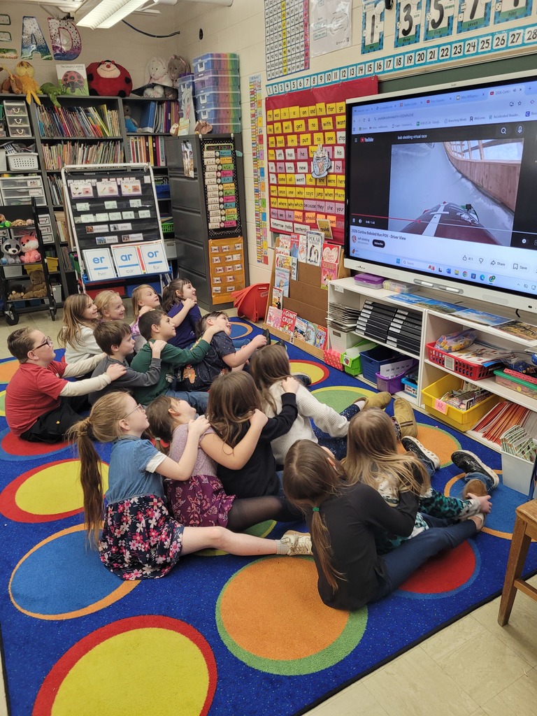 Students are sitting in groups of 2 and four. They have their arms on the person in front of them and their legs on the person's side. They are leaning the direction of the track as they follow a first person POV of a race.