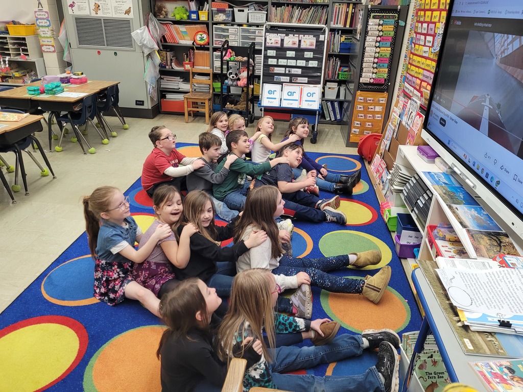 Students are sitting in groups of 2 and four. They have their arms on the person in front of them and their legs on the person's side. They are leaning the direction of the track as they follow a first person POV of a race.