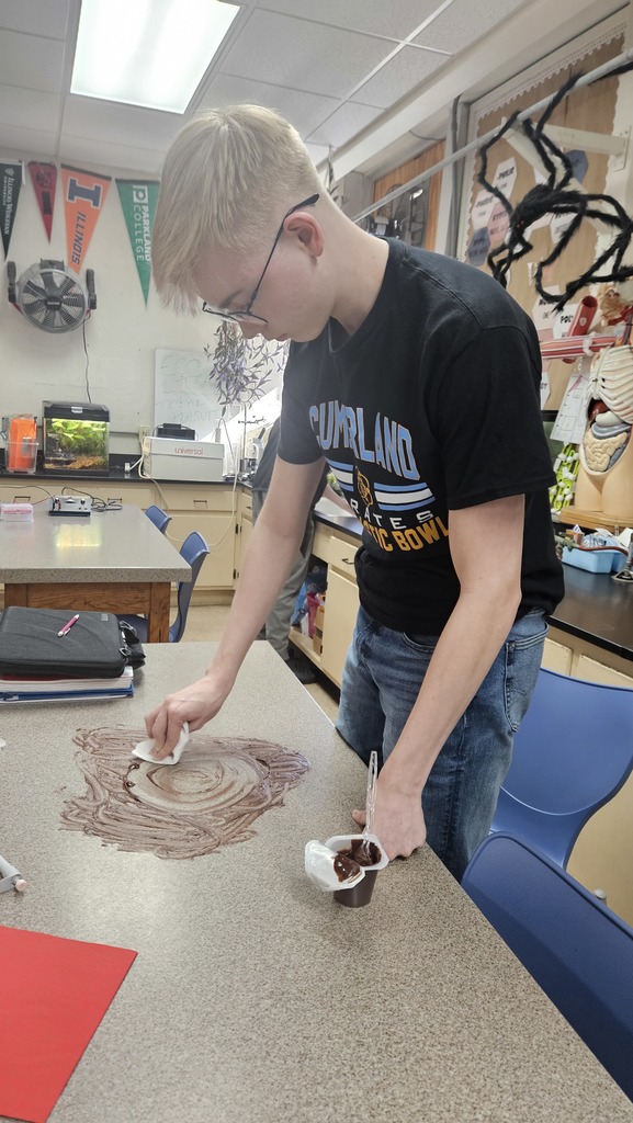 With pudding smeared on the table, a student is using circular motions to wipe up the pudding. 