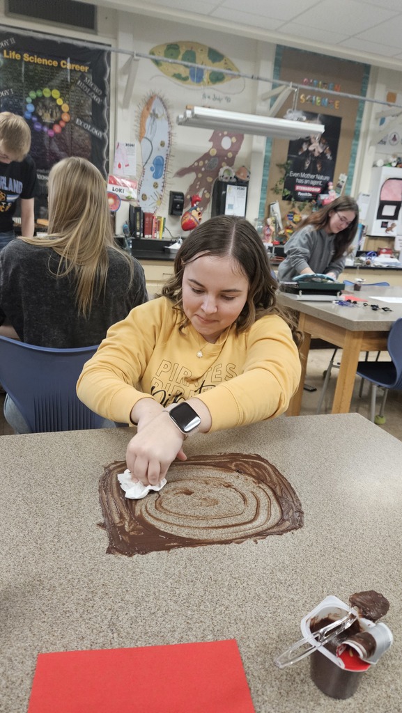 With pudding smeared on the table, a student is using circular motions to wipe up the pudding. 