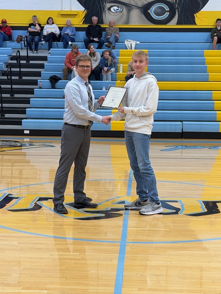Pictured is CJ accepting the certificate from Mr. Huffman, Principal, at center court. They are shaking hands and holding the certificate. 
