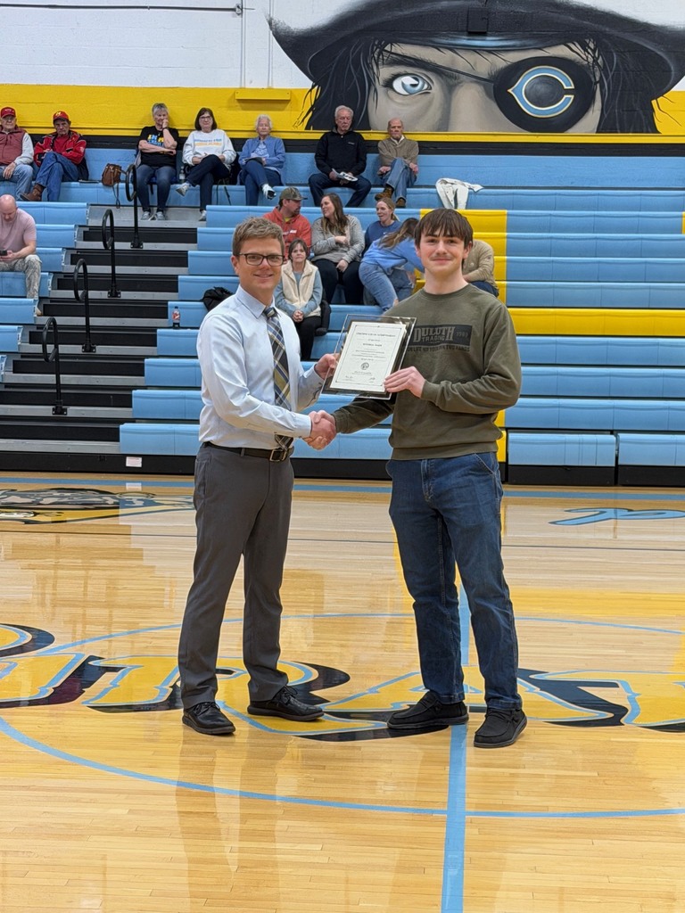 Pictured is MB accepting the certificate from Mr. Huffman, Principal, at center court. They are shaking hands and holding the certificate. 
