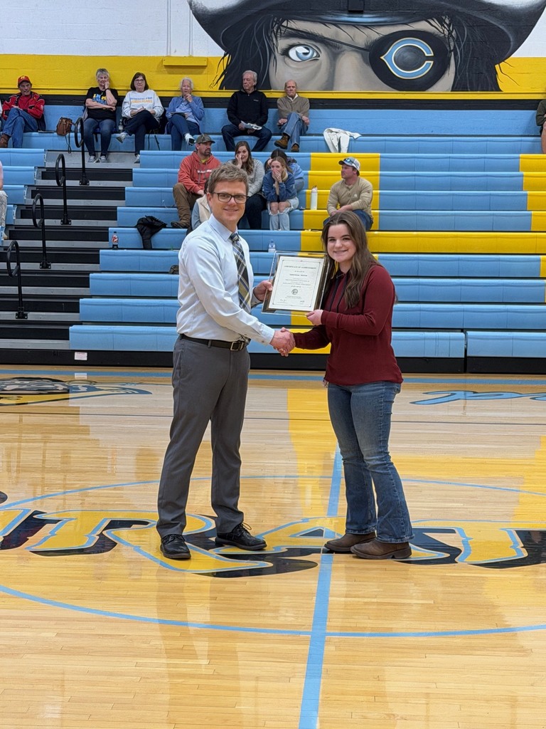 Pictured is GH accepting the certificate from Mr. Huffman, Principal, at center court. They are shaking hands and holding the certificate. 