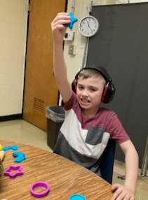 A student is holding up a playdoh star that he made as a speech activity.