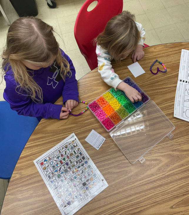 Two students are creating a bracelet as a speech activity.