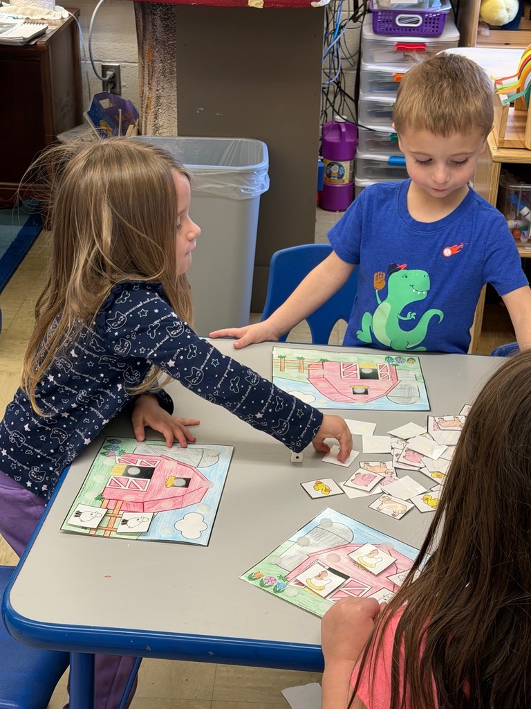Two students are sitting at a table where they are rolling a dice and velcroing animals to their farm scene. 